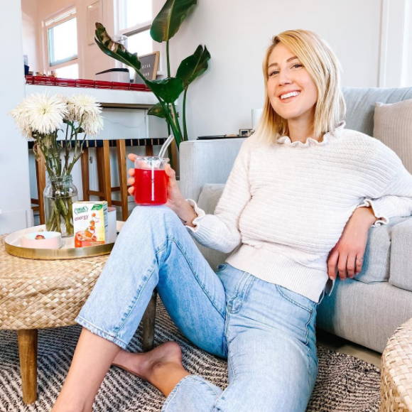 Blonde woman in white shirt and jeans sitting on floor drinking True Lemon Strawberry Dragonfruit drink