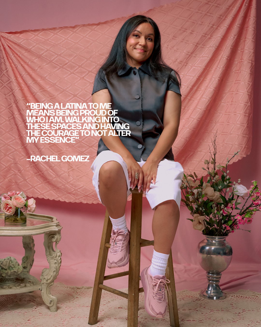 Person sitting on a stool, wearing a shirt and shorts, with a pink background.