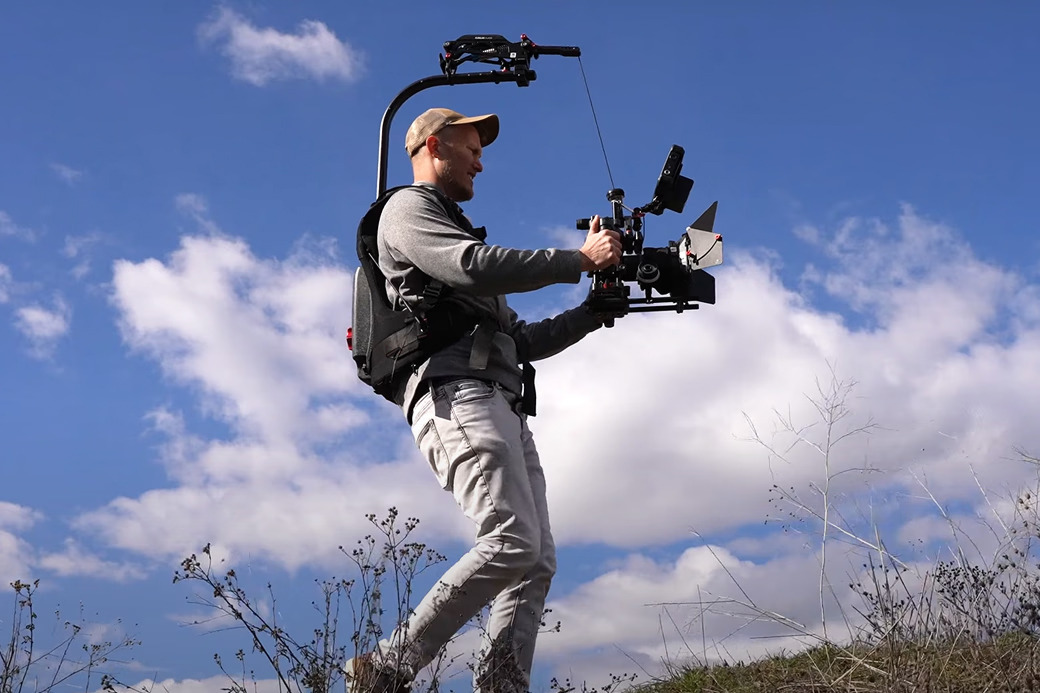 Person filming outdoors with a camera on a stabilizer, blue sky in background.