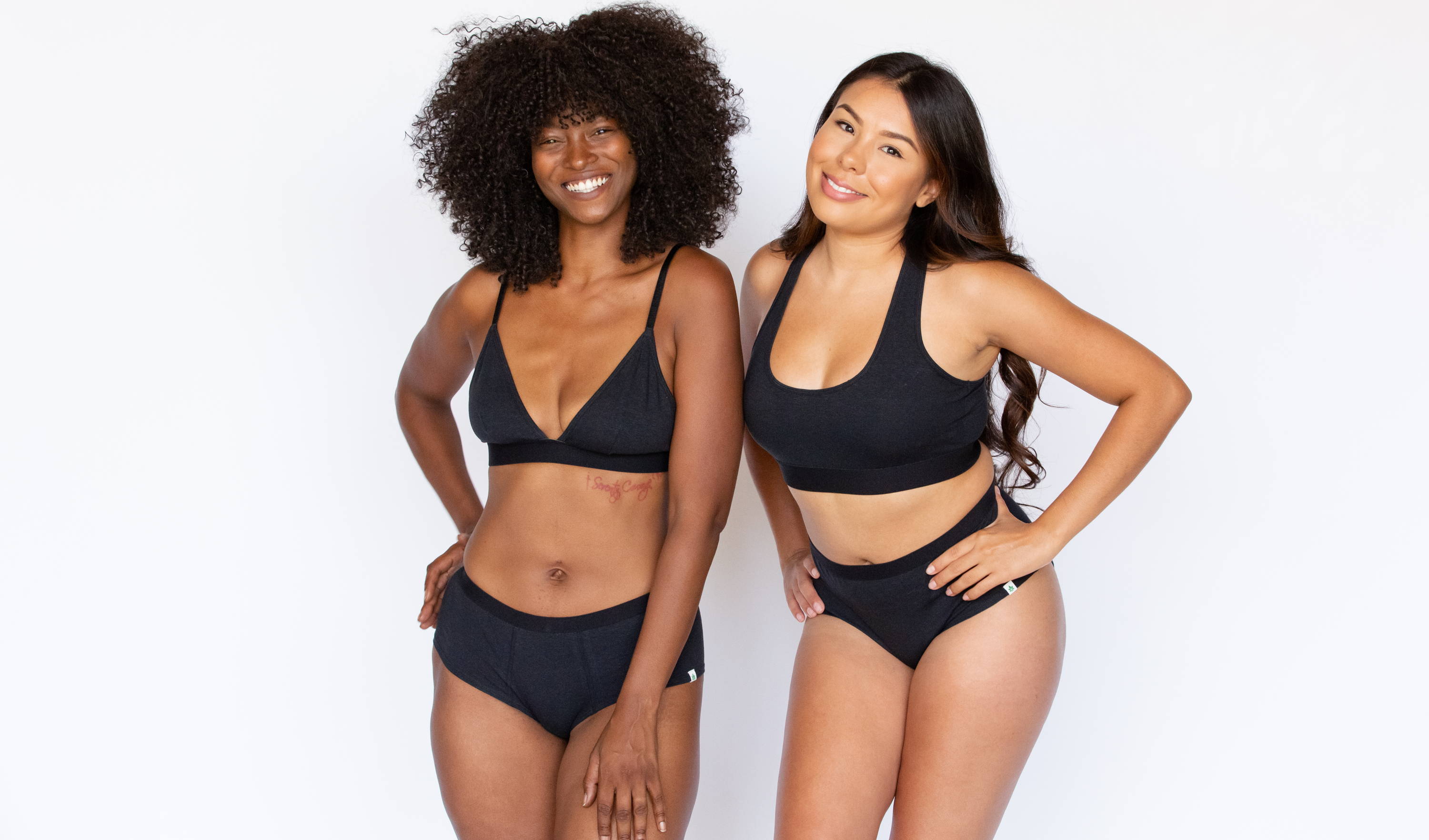 Two women stand in WAMA hemp bralettes with their hands on their hips.