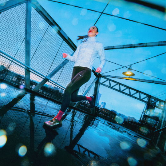 Person running on a bridge during a rainy evening, with a blue background.