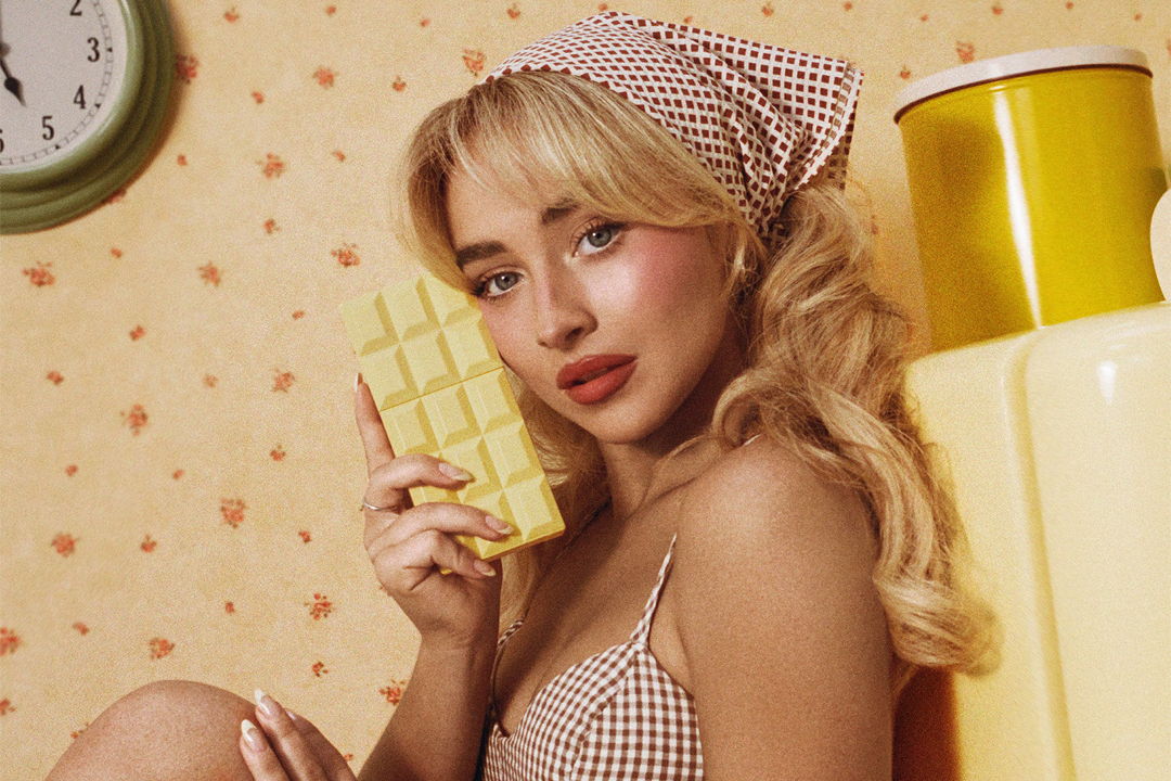 Woman holding a yellow chocolate bar, wearing a checked outfit and headscarf.