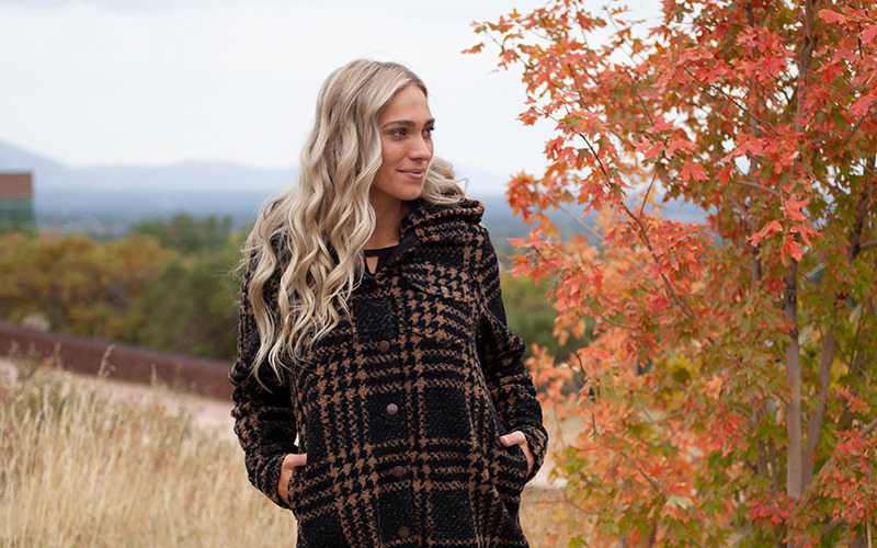 Woman standing in fall field wearing brown Ashlyn jacket.