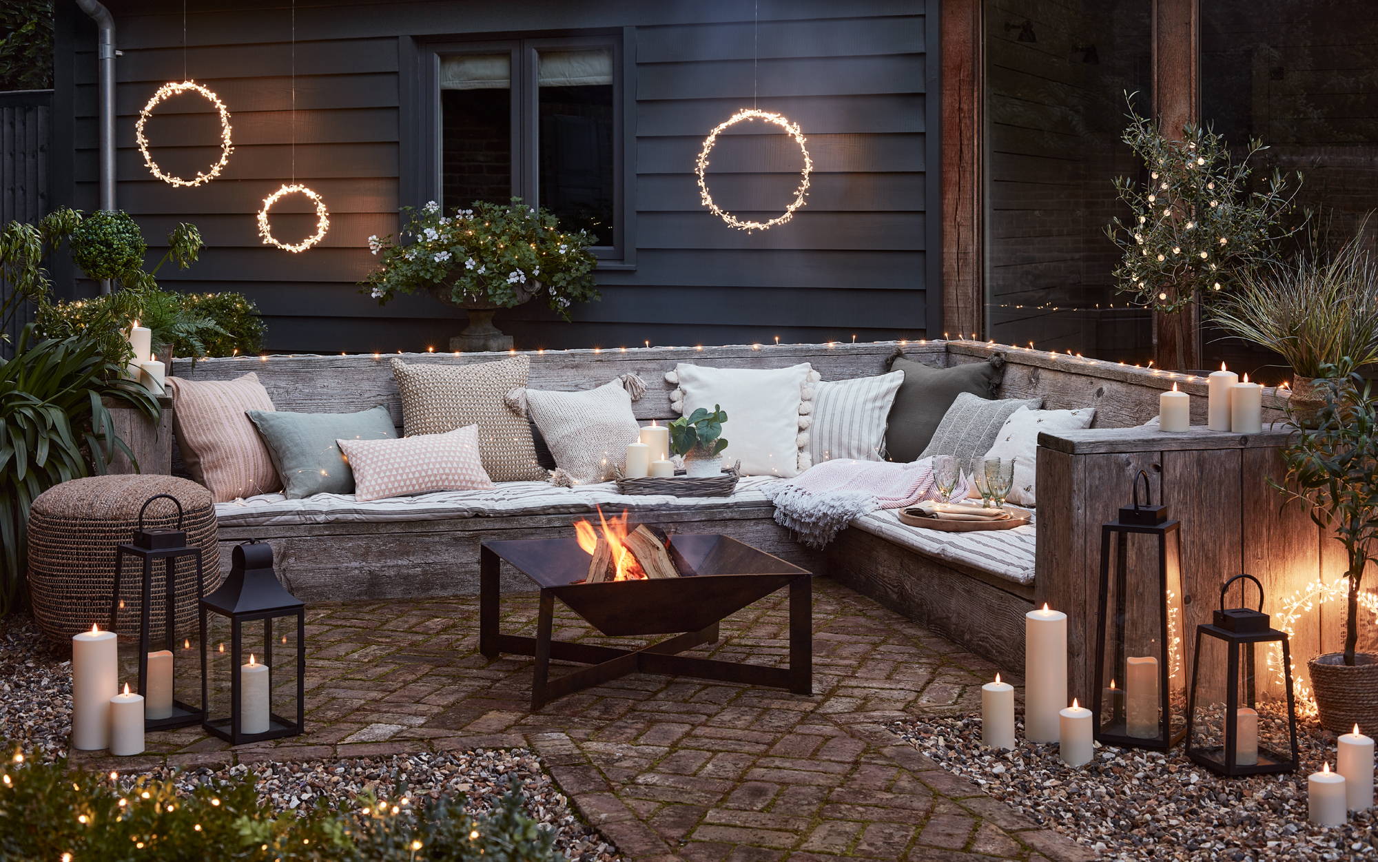 Ein Sitzbereich im Garten dekoriert mit LED Kerzen, Laternen und leuchtenden Kreisen mit einer Feuerschale im Vordergrund