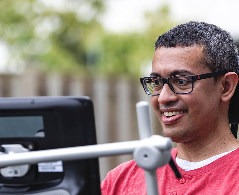 Un homme en fauteuil roulant sourit devant un dispositif de communication.