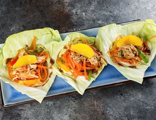 Three lettuce wraps filled with colorful vegetables and protein on a blue plate.