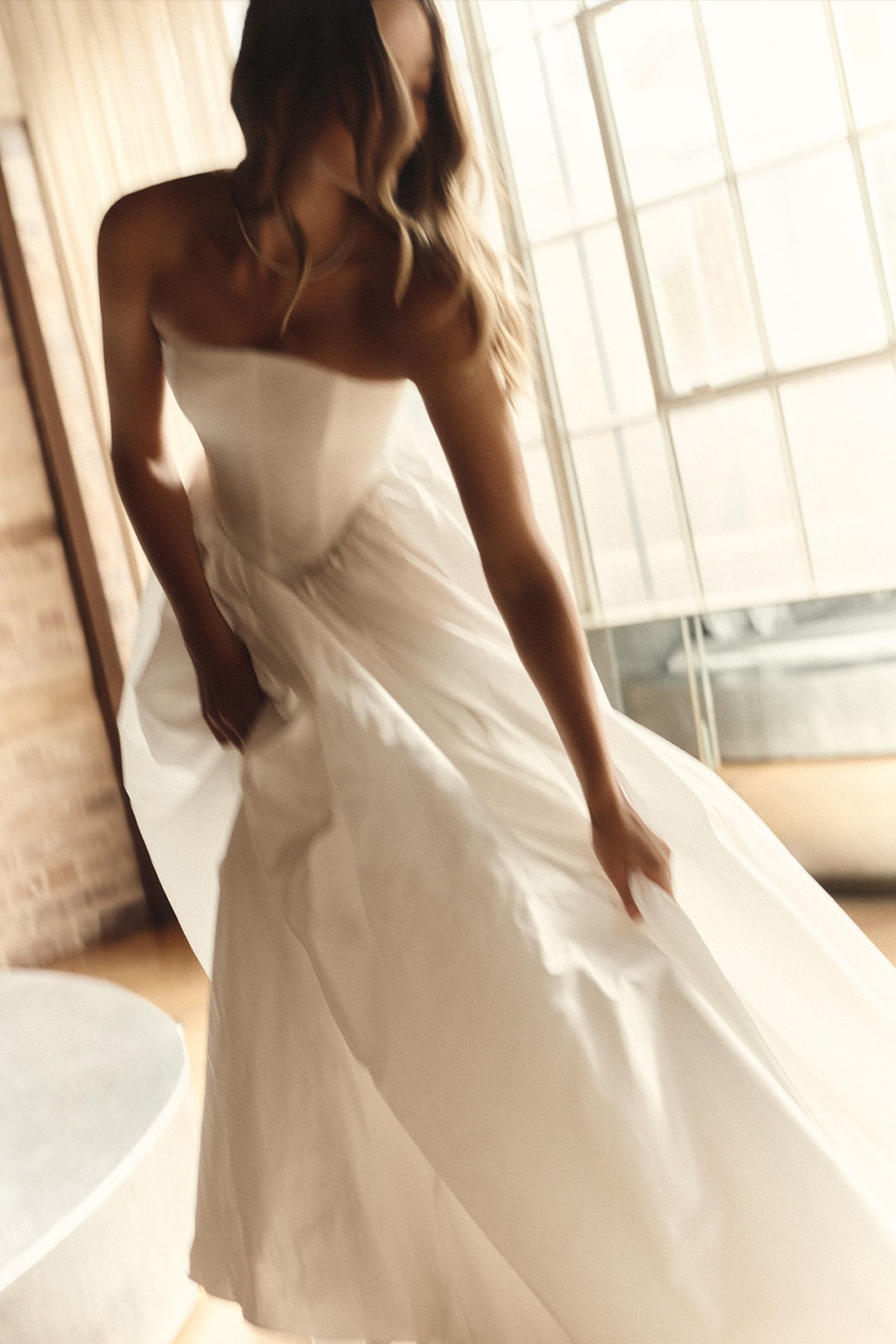 Woman in a flowing white dress, posing in a bright indoor setting.