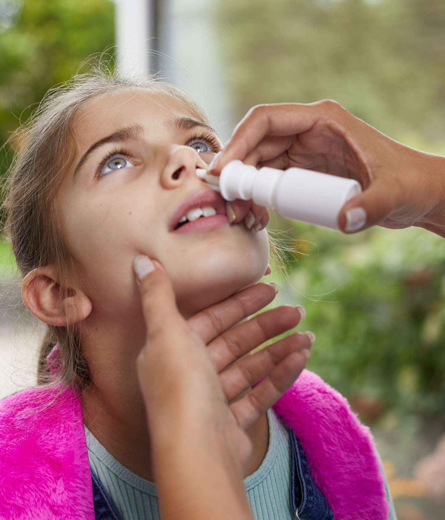 Child tipping her back as her mother gives her a dose of corticosteroid nasal spray to ease a stuffy runny nose from allergies