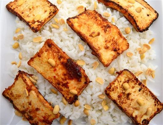 Grilled tofu slices served on a bed of rice with peanuts.