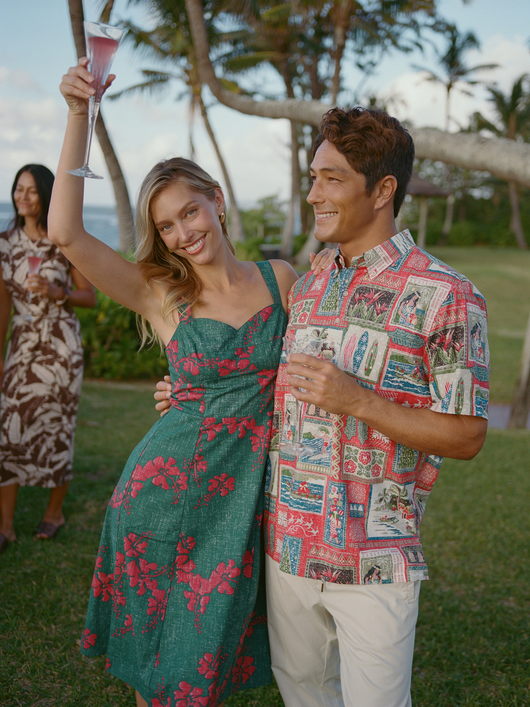 Two people celebrating outdoors, holding drinks, with a tropical background.