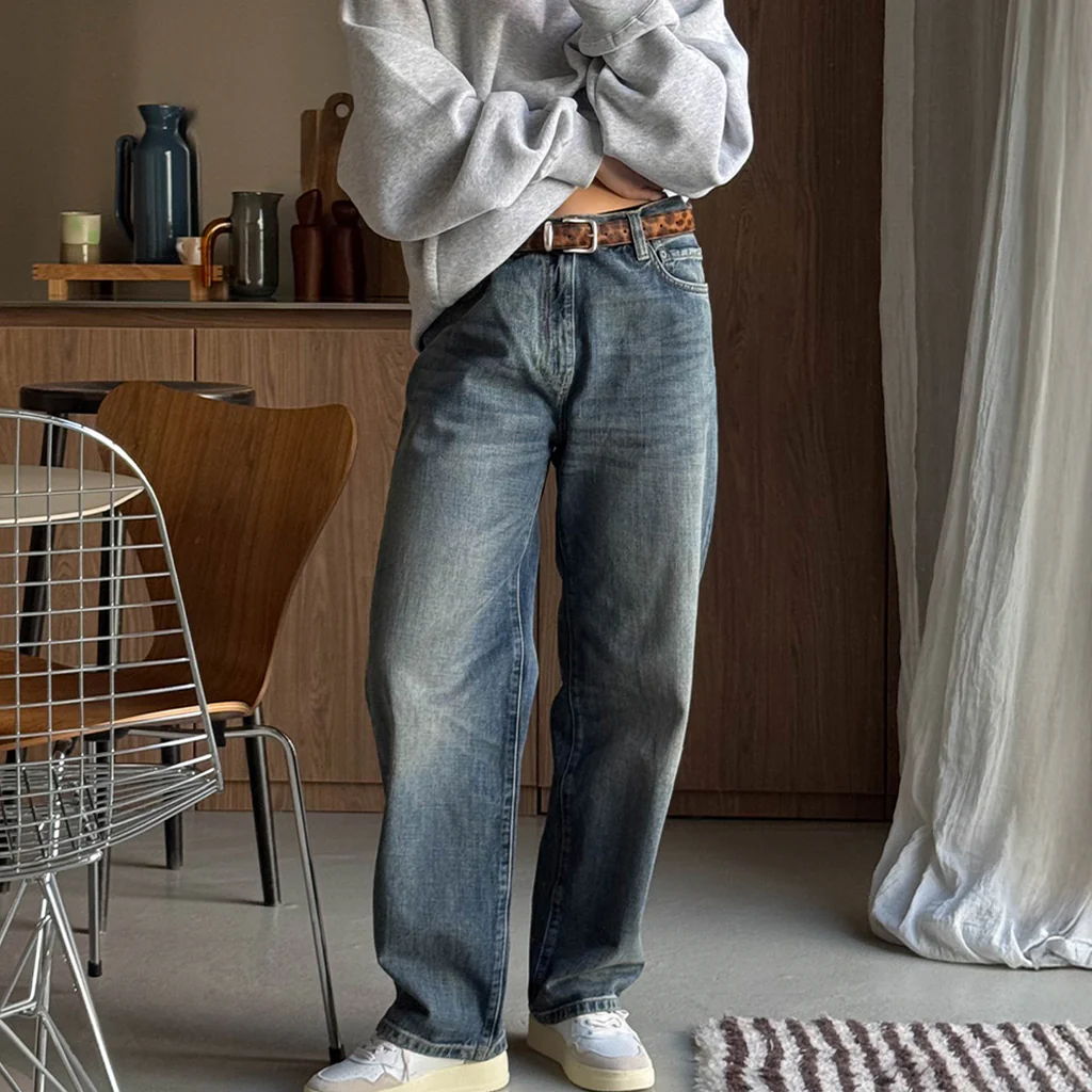 Person wearing oversized gray sweater and jeans in a stylish indoor setting.