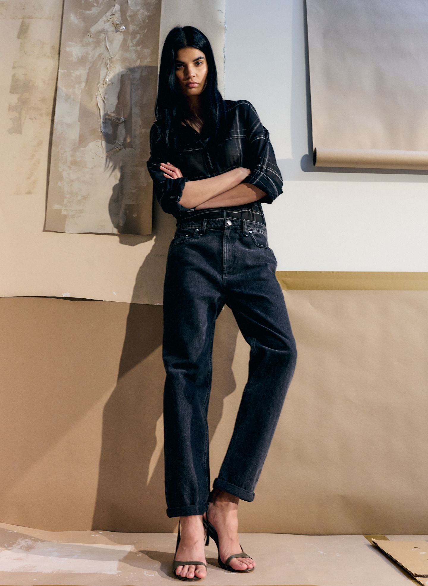Model in stylish black outfit posing against a textured background.
