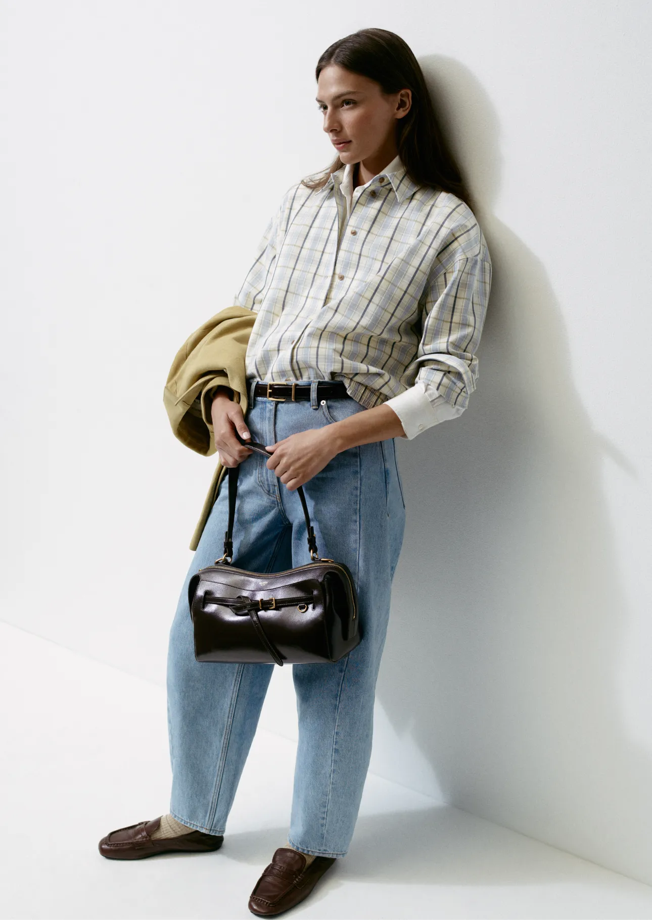 Woman in a plaid shirt and loose jeans holding a handbag.
