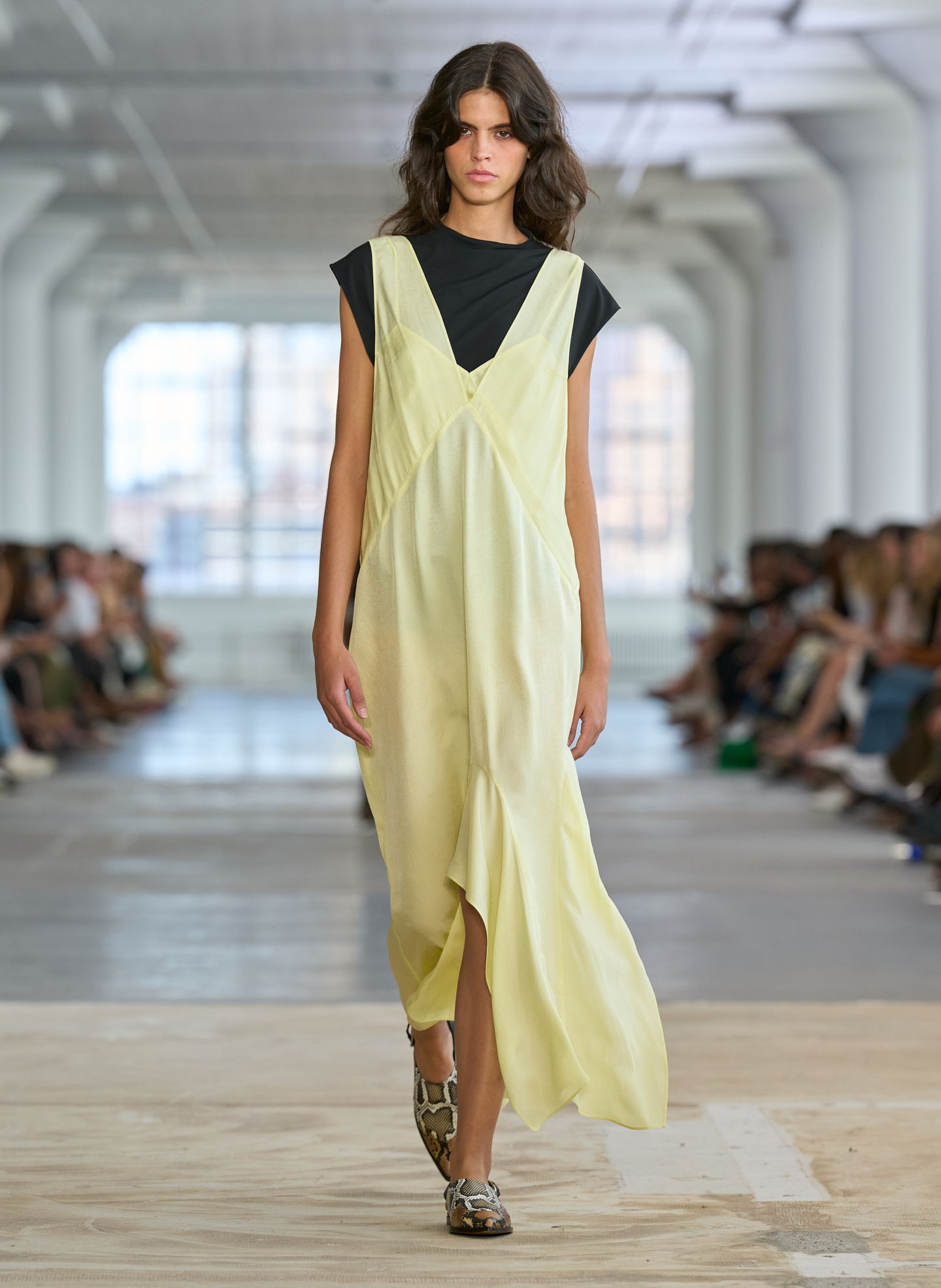 Model walking down runway in a yellow dress and black top.