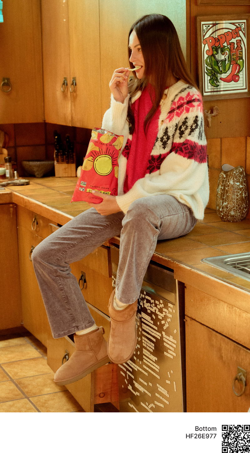 Young woman sitting on a kitchen counter enjoying snacks in cozy attire.