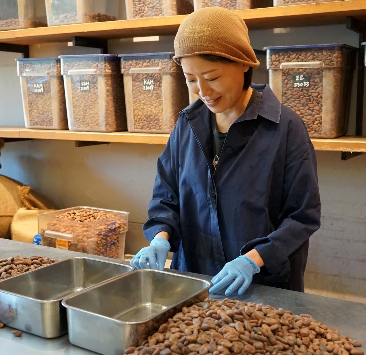 Woman sorting chocolate beans in a workspace with containers.