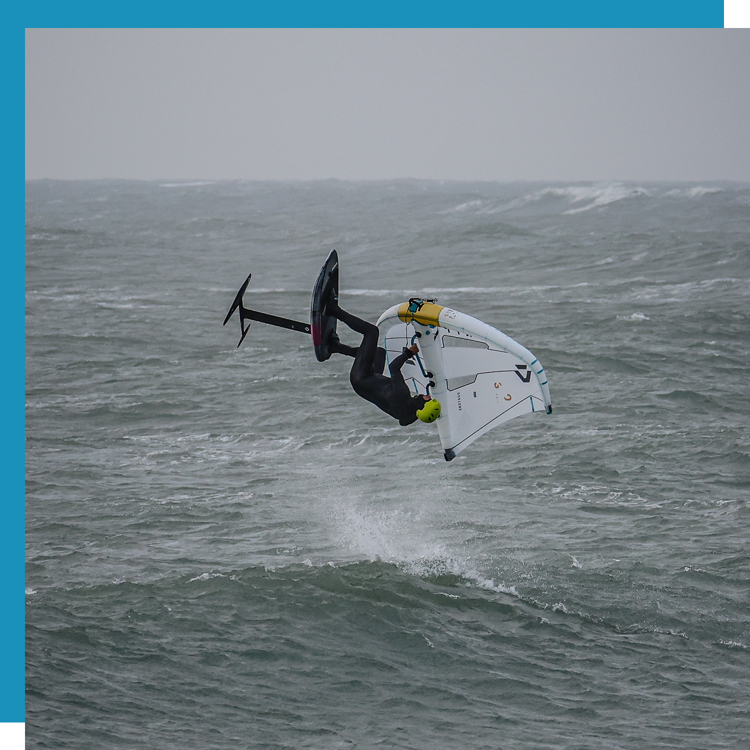Person performing a trick on a wingfoil board in rough water.