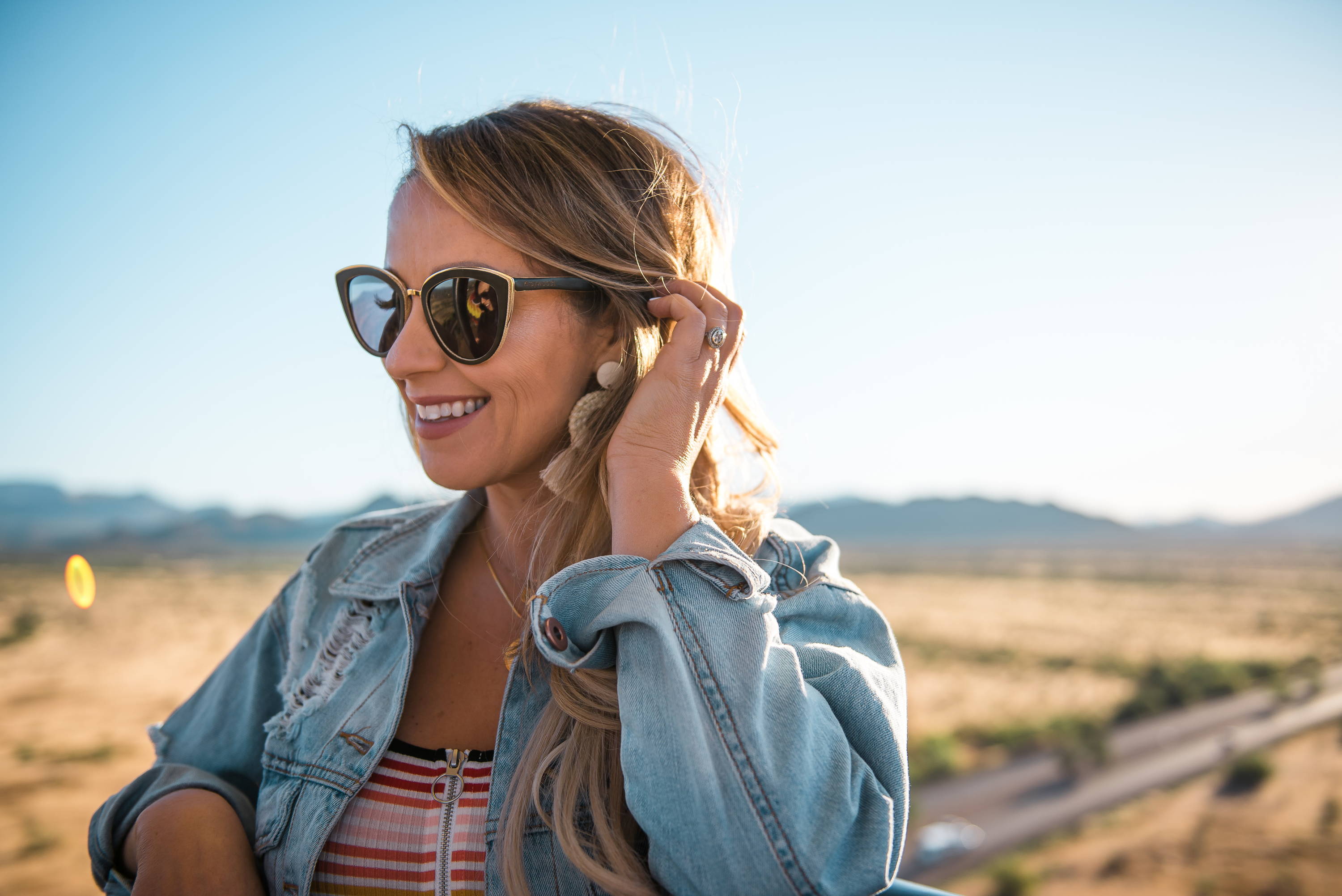 Femme portant des lunettes de soleil en bois Willow, Cat-Eye avec lentille polarisée grise avec une chemise stipped et une veste en jean debout en plein air