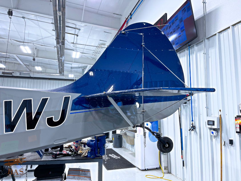 Blue aircraft tail in a hangar with equipment and screens visible.