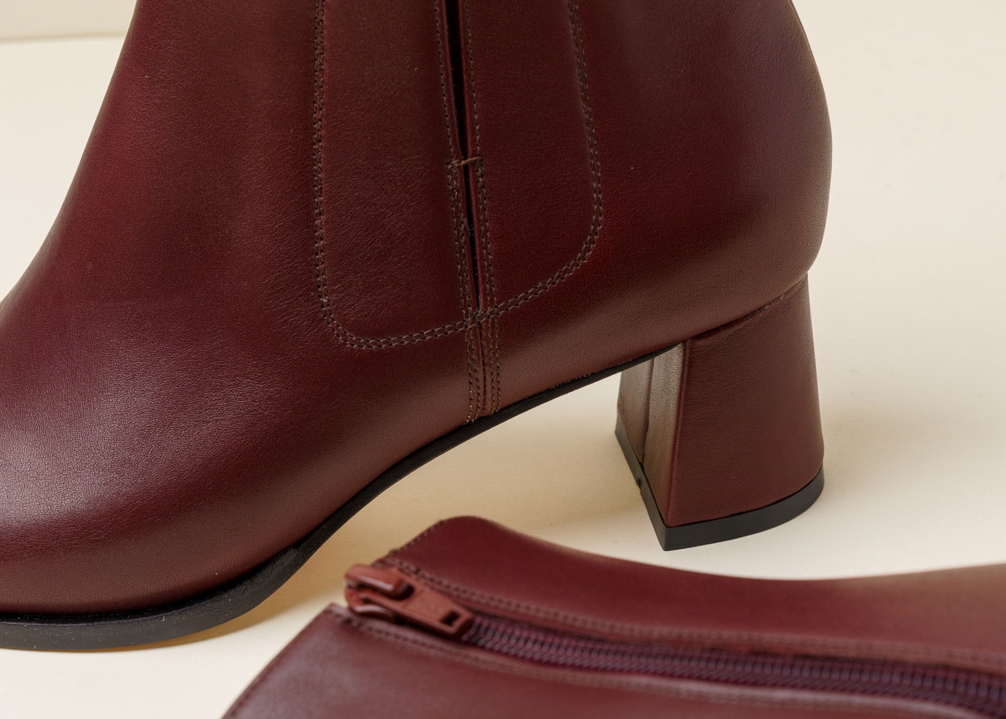 Burgundy leather ankle boots with a block heel on a neutral background.