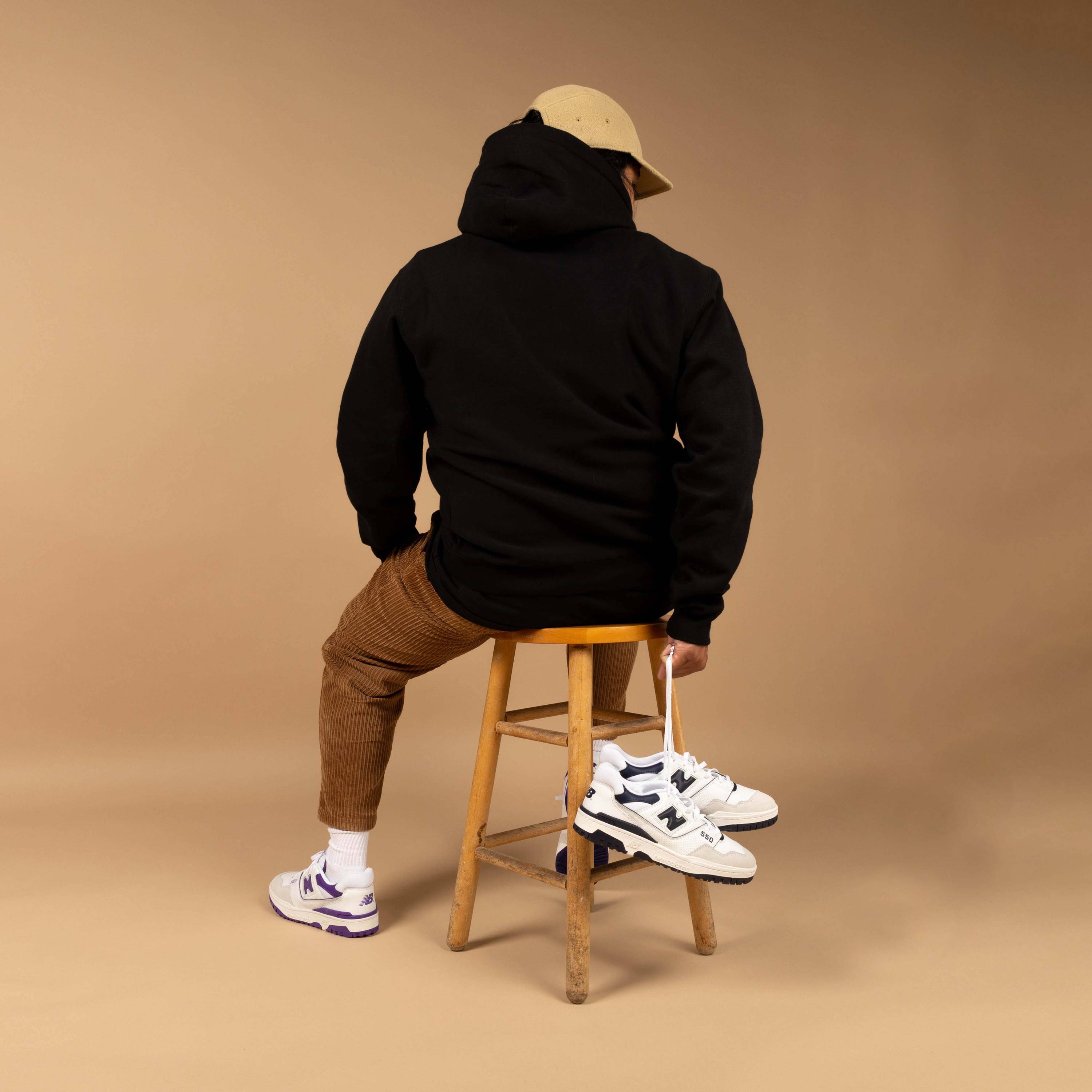 male model holding new balance 550 shoes by laces while sitting on barstool