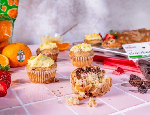Colorful cupcakes surrounded by fruits and snacks on a pink table.