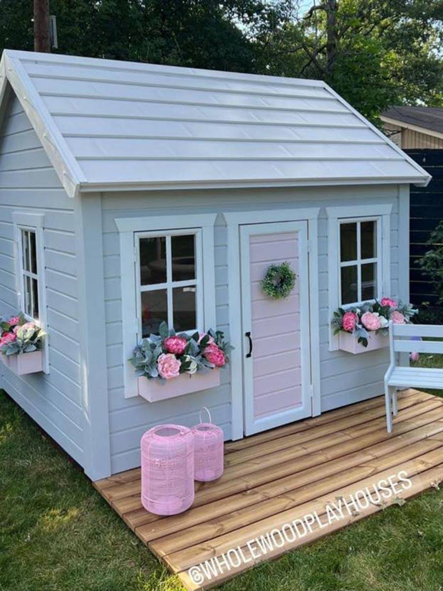 Kids Playhouse Natural Wonder in Garden, View from Left, showing Three Windows with pink Flower Boxes and pink front door by WholeWoodPlayhouses 