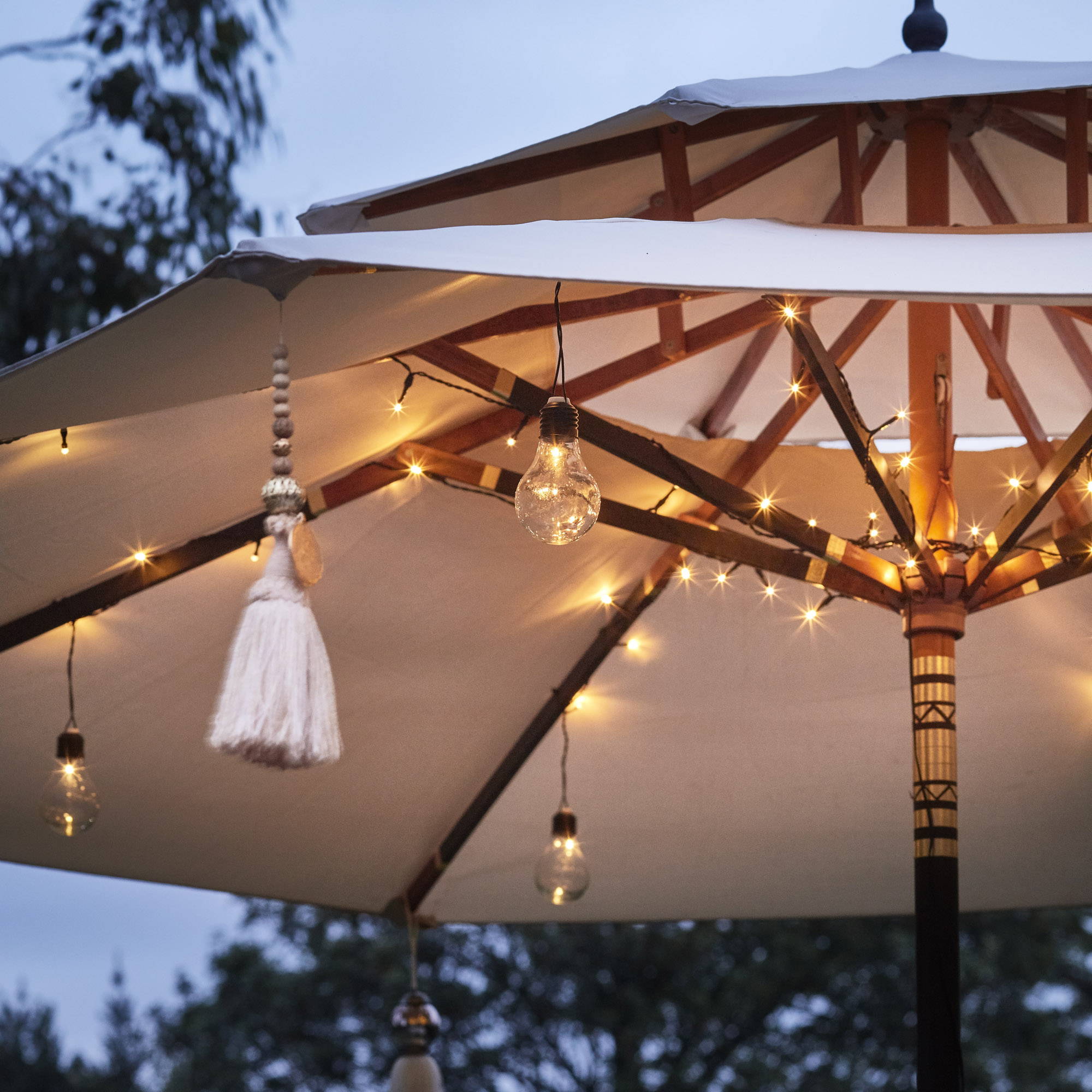 A parasol with fairy  lights and festoon lights hanging from the inside. 