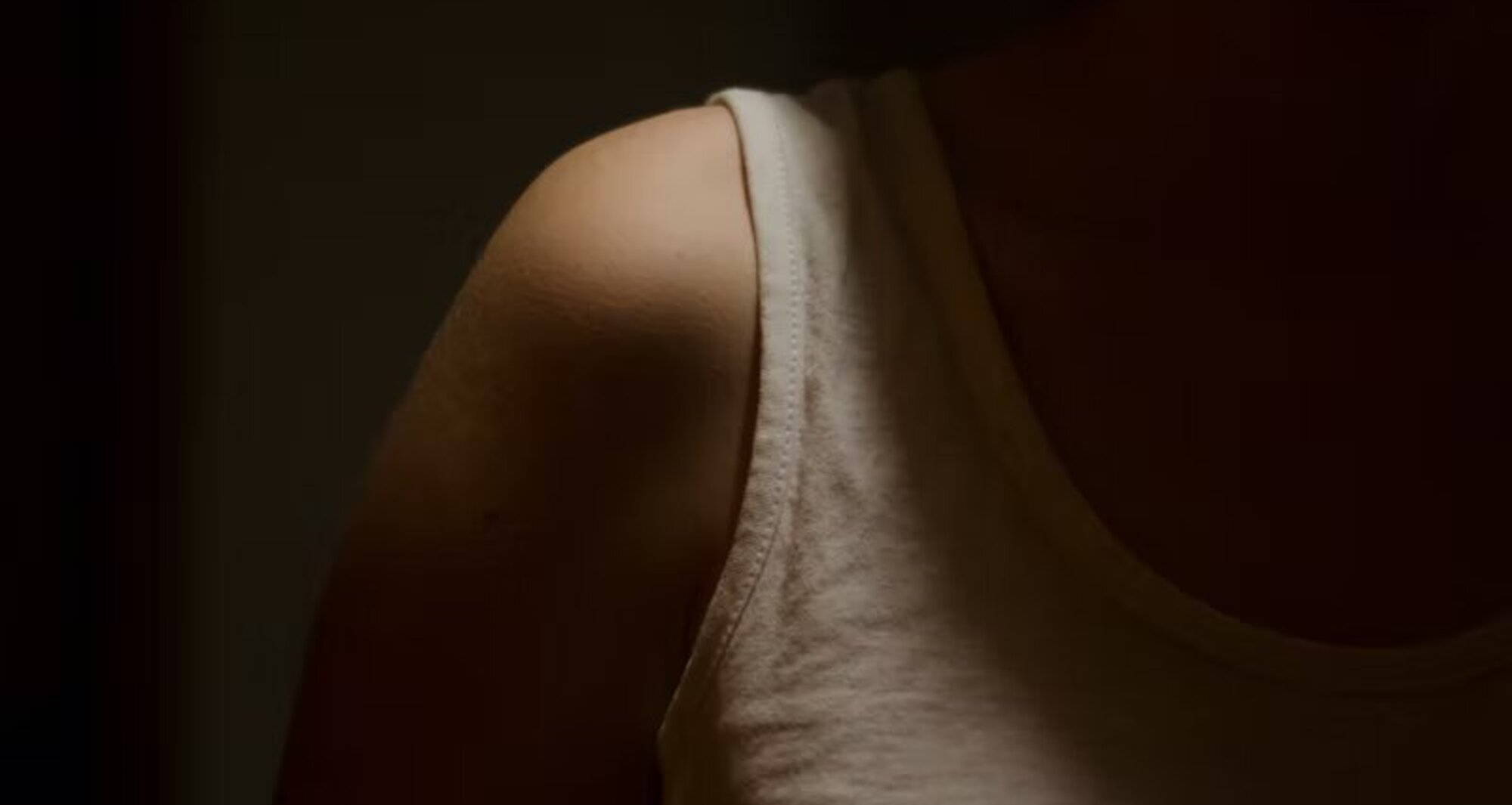 a shoulder lit up against a dark background wearing a white cotton tank top