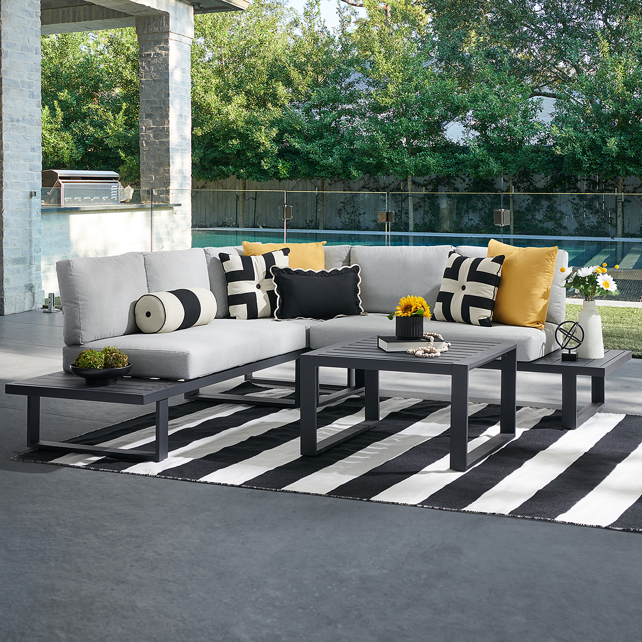 Outdoor seating area with gray cushions, black and white rug, and decorative pillows.