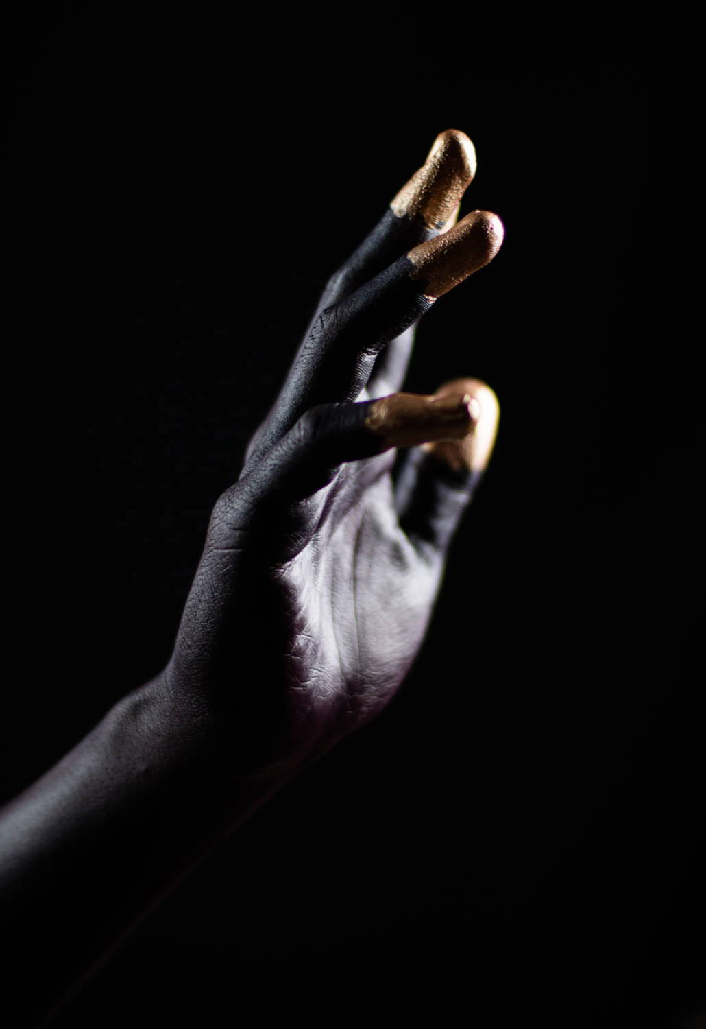 Hand in near darkness. Gold fingertips.