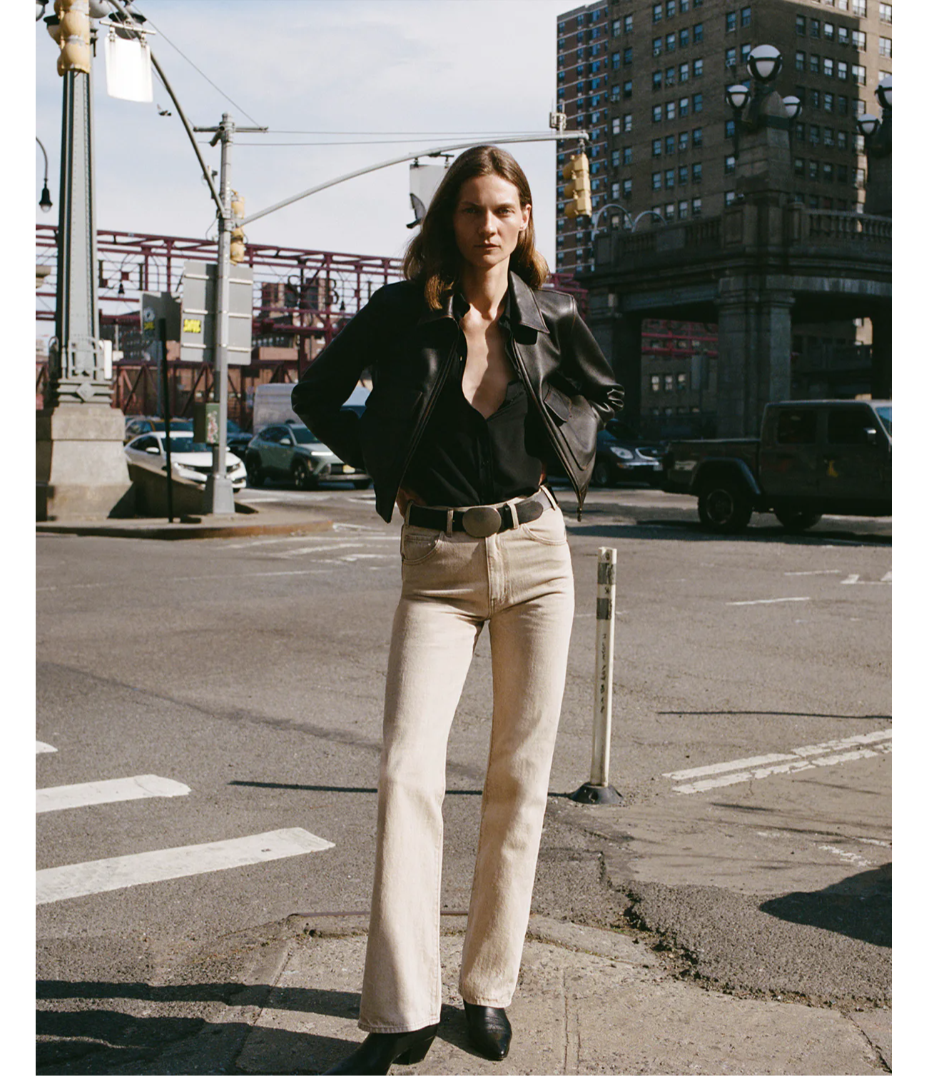 A person in a black jacket and beige pants standing on a city street.