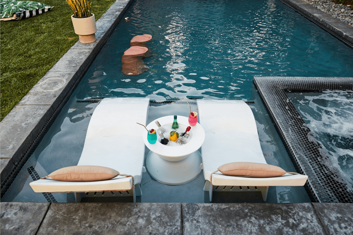 A pool with chaise loungers, ice bin side table, and bar stools.