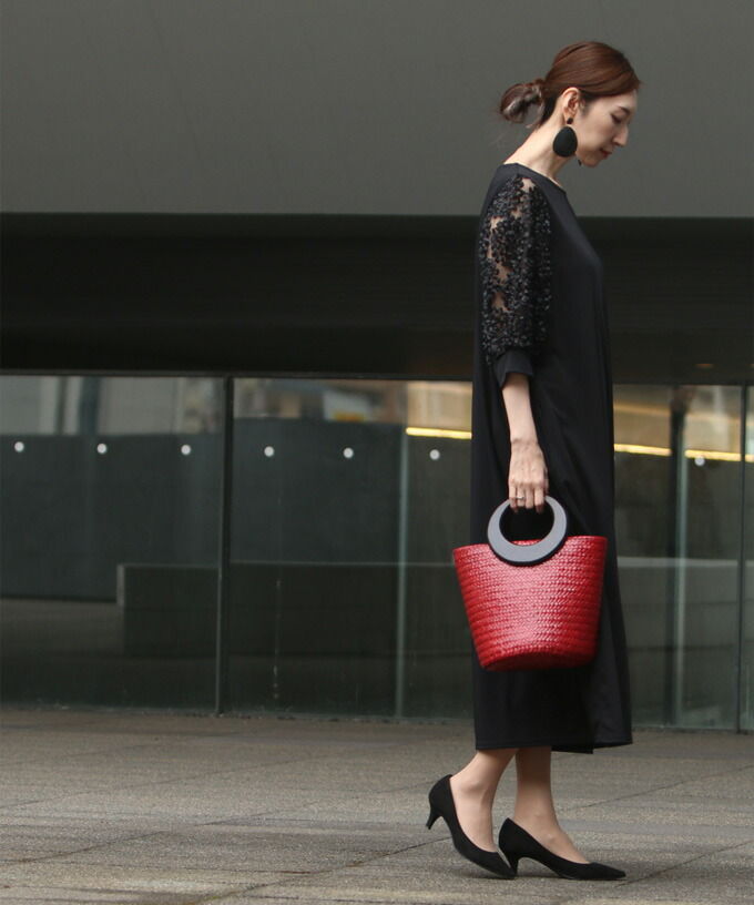 Woman in black dress holding a red handbag, walking outdoors.