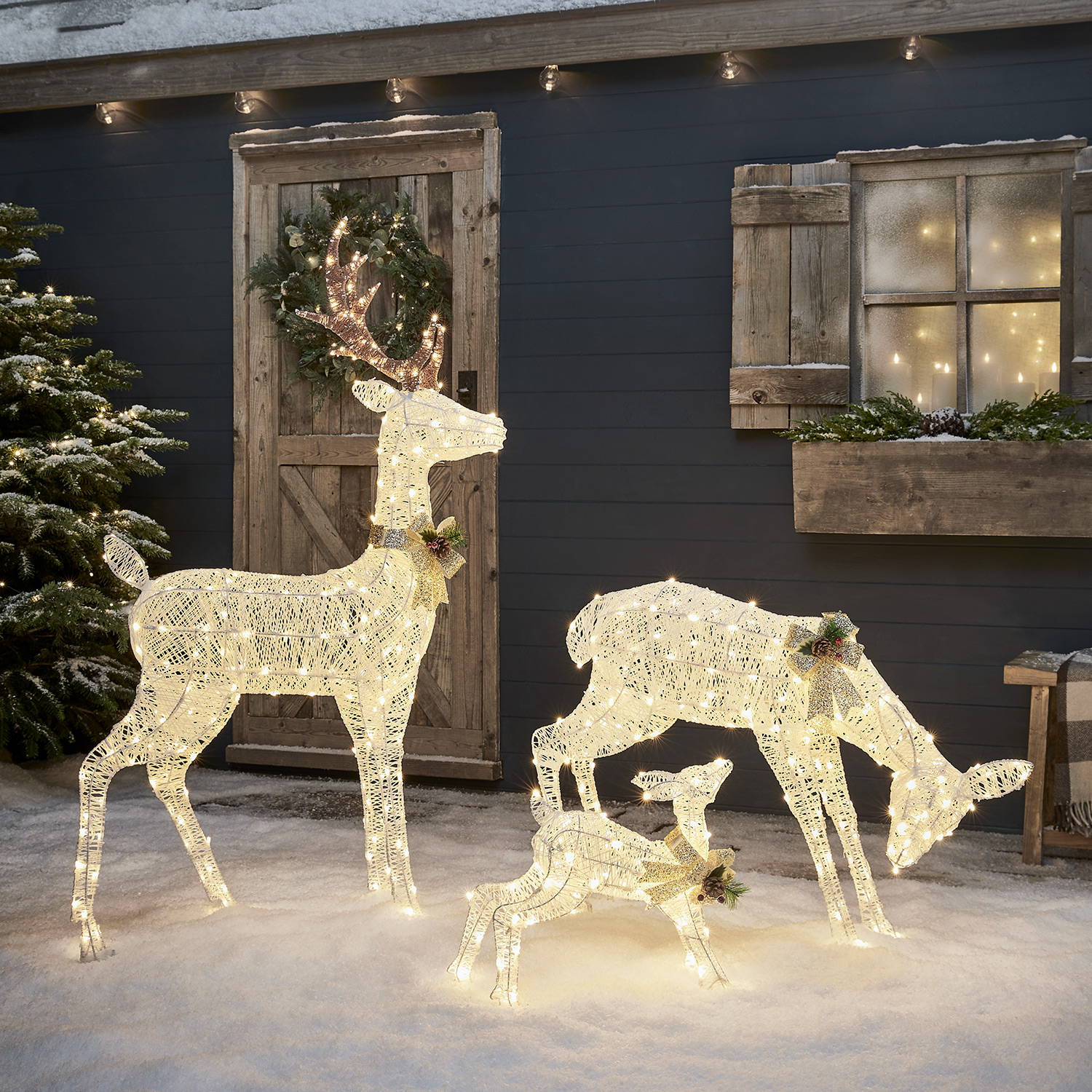 White spun cotton light up reindeer family outside a Winter cabin with snow.
