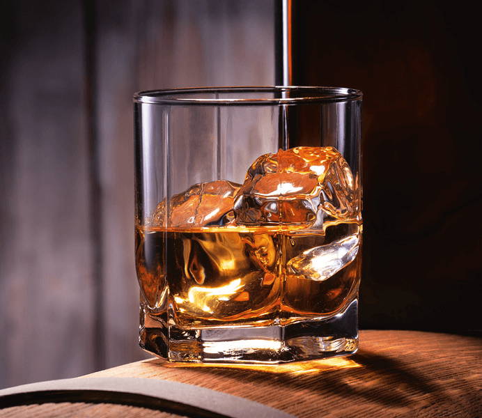 Ein Glas Whisky mit Eis auf einem Fass