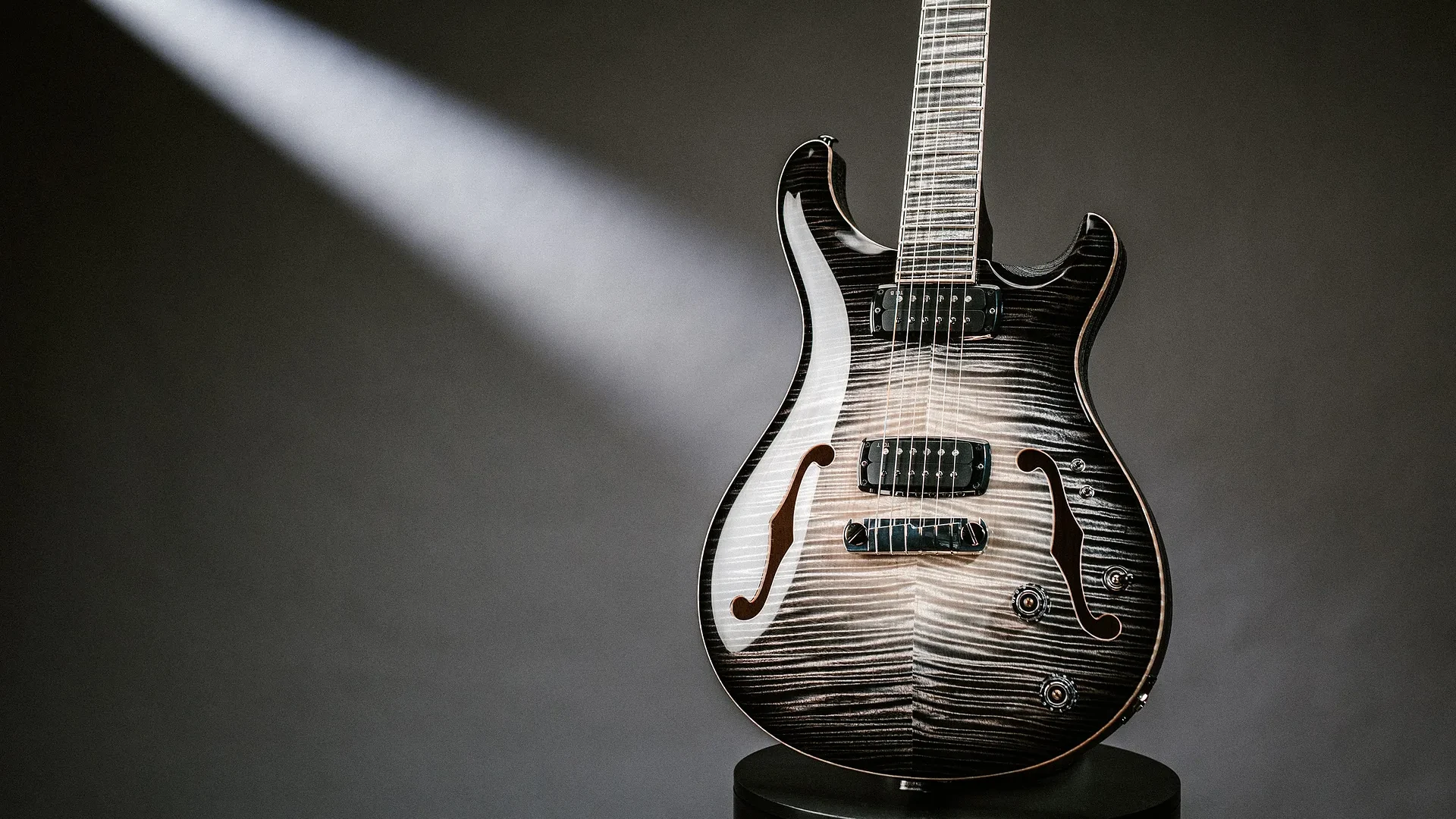 A stylish PRS Private Stock electric guitar illuminated by a spotlight on a dark background.