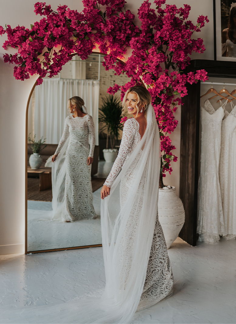 Bride in a stunning dress, surrounded by vibrant pink flowers and mirrors.