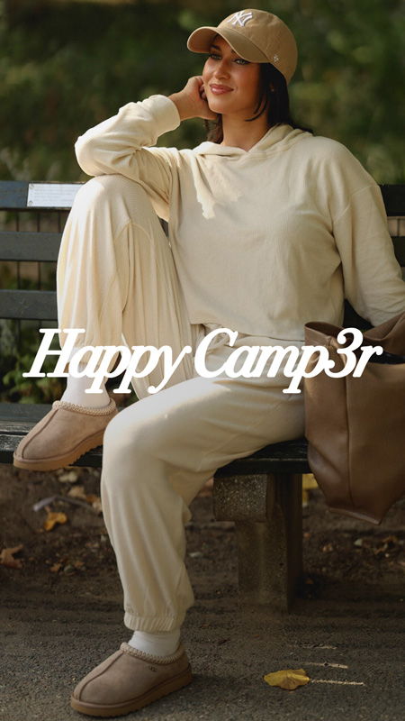 Person in casual outfit sitting on a bench, wearing a cap and smiling.