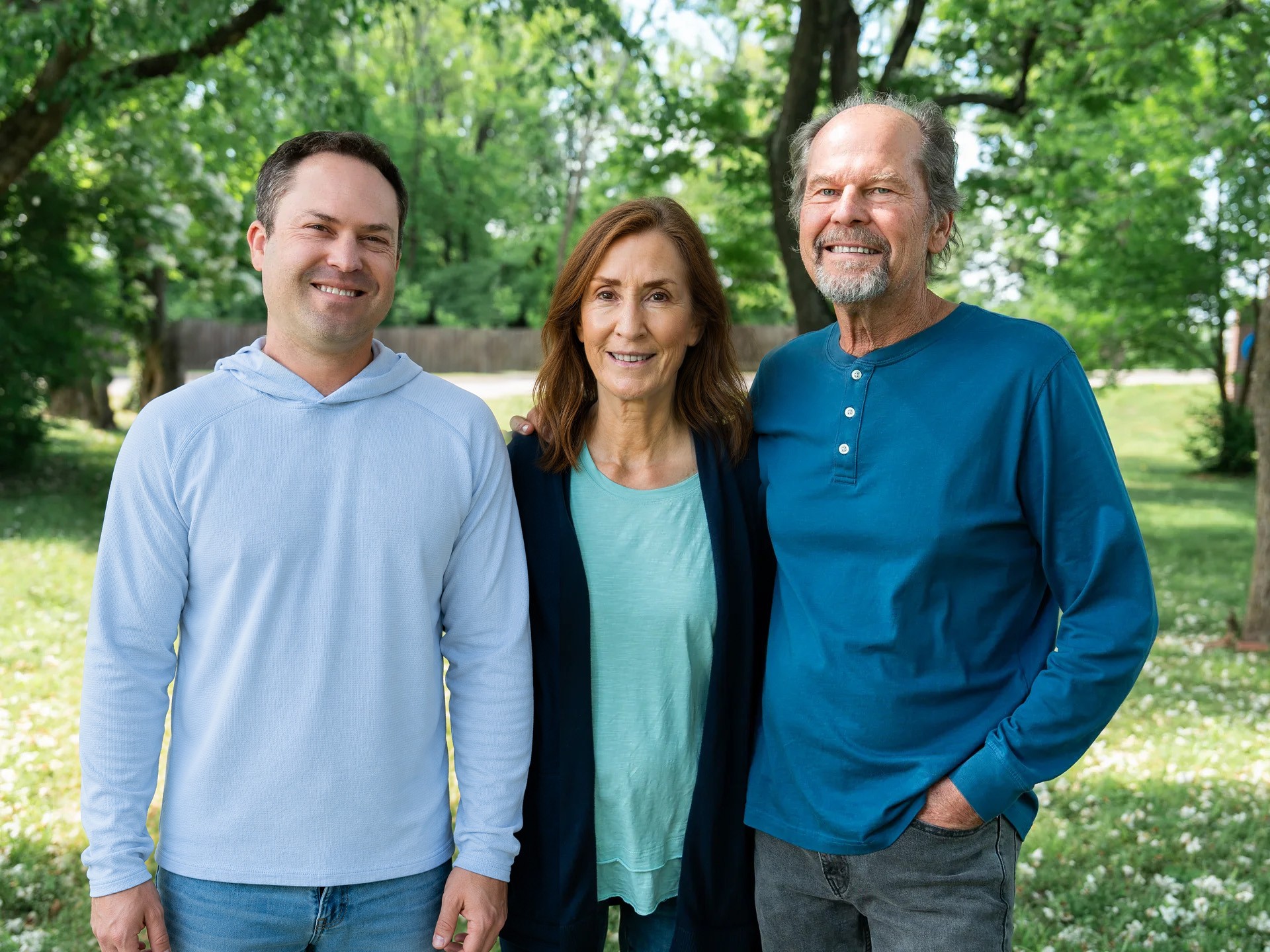 Three people standing together outdoors in a green, grassy area.