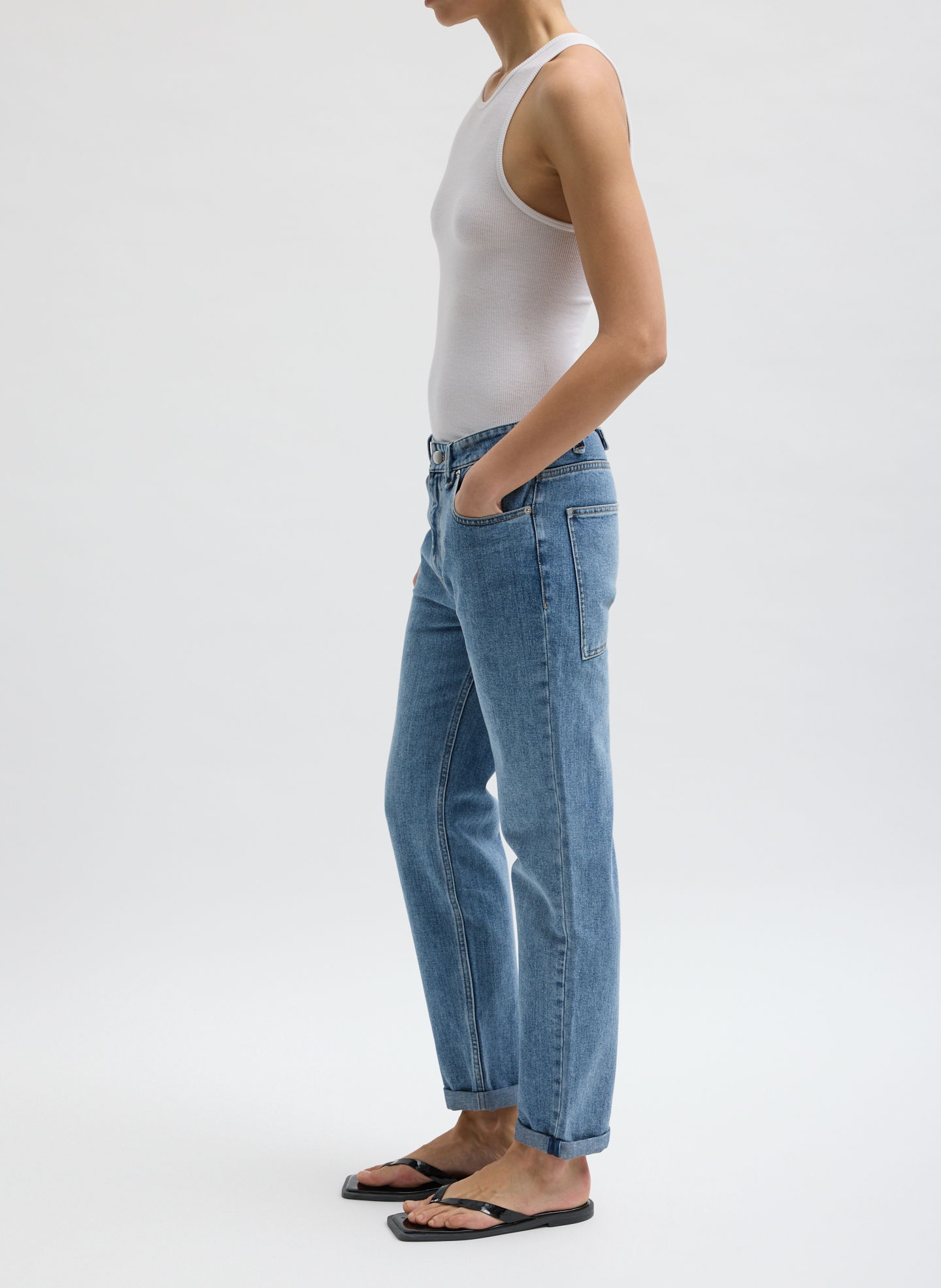 Person wearing a white tank top and blue jeans, standing sideways.