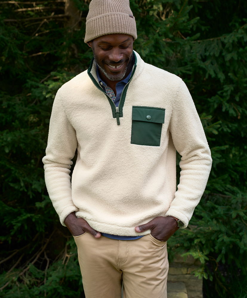 Man smiling in a cream pullover and beige pants, standing in nature.