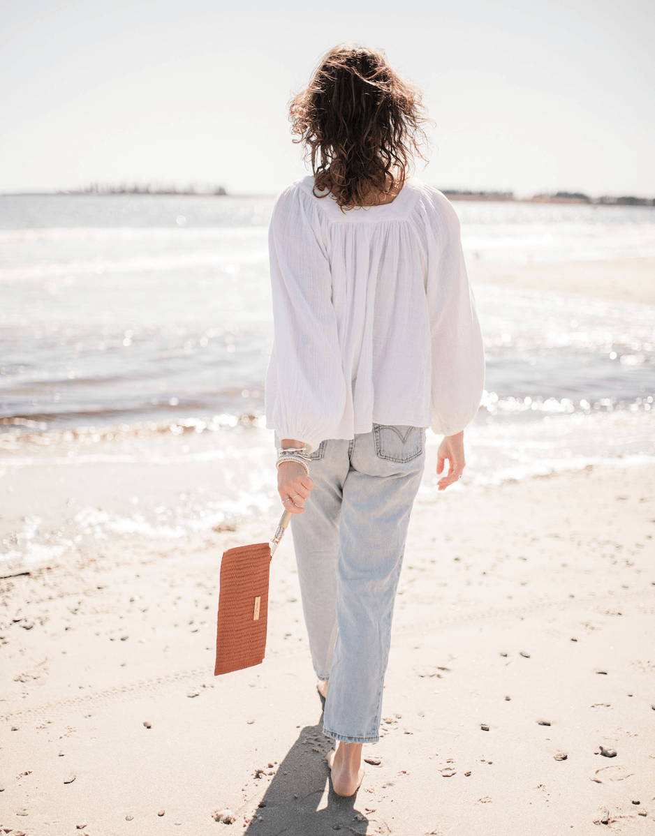 woman walking into the ocean with a clutch
