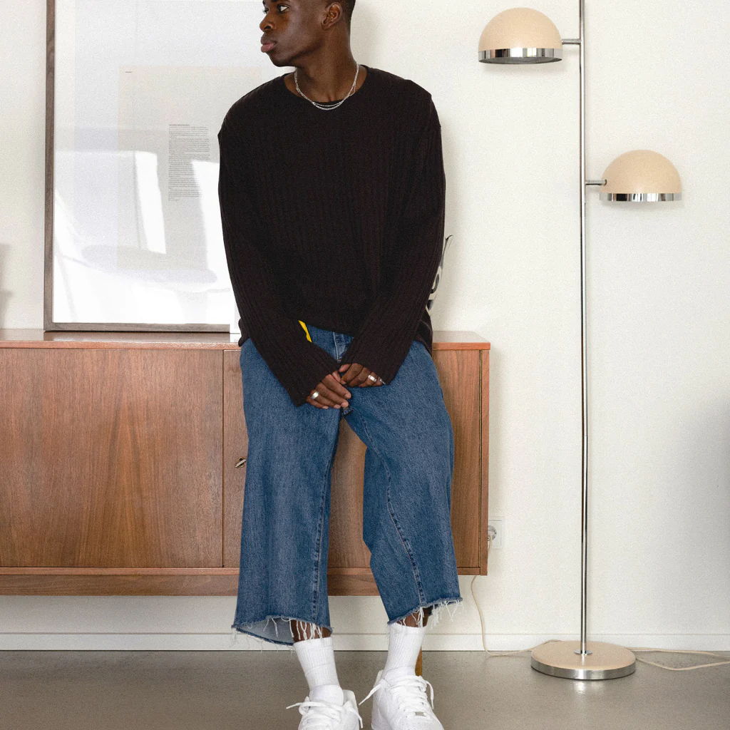 Person standing in a room, wearing a black sweater and blue jeans.