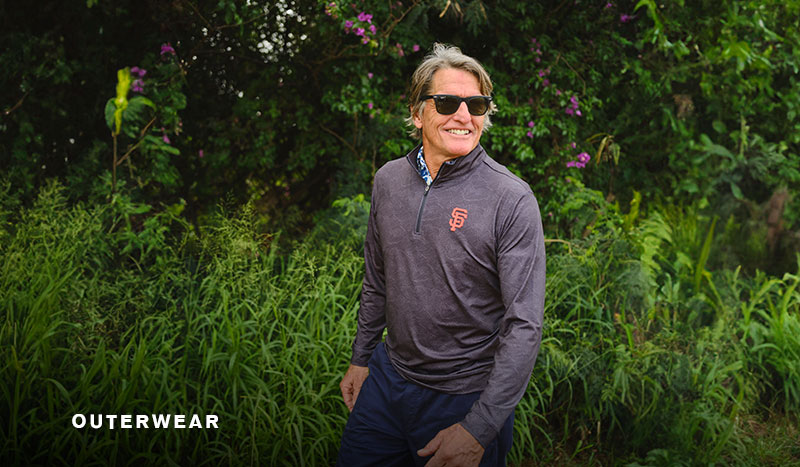 Man in sunglasses wearing a gray outerwear shirt in a green landscape.