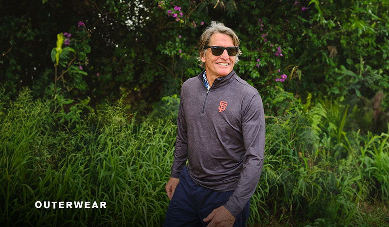 Man in sunglasses wearing a gray outerwear shirt in a green landscape.