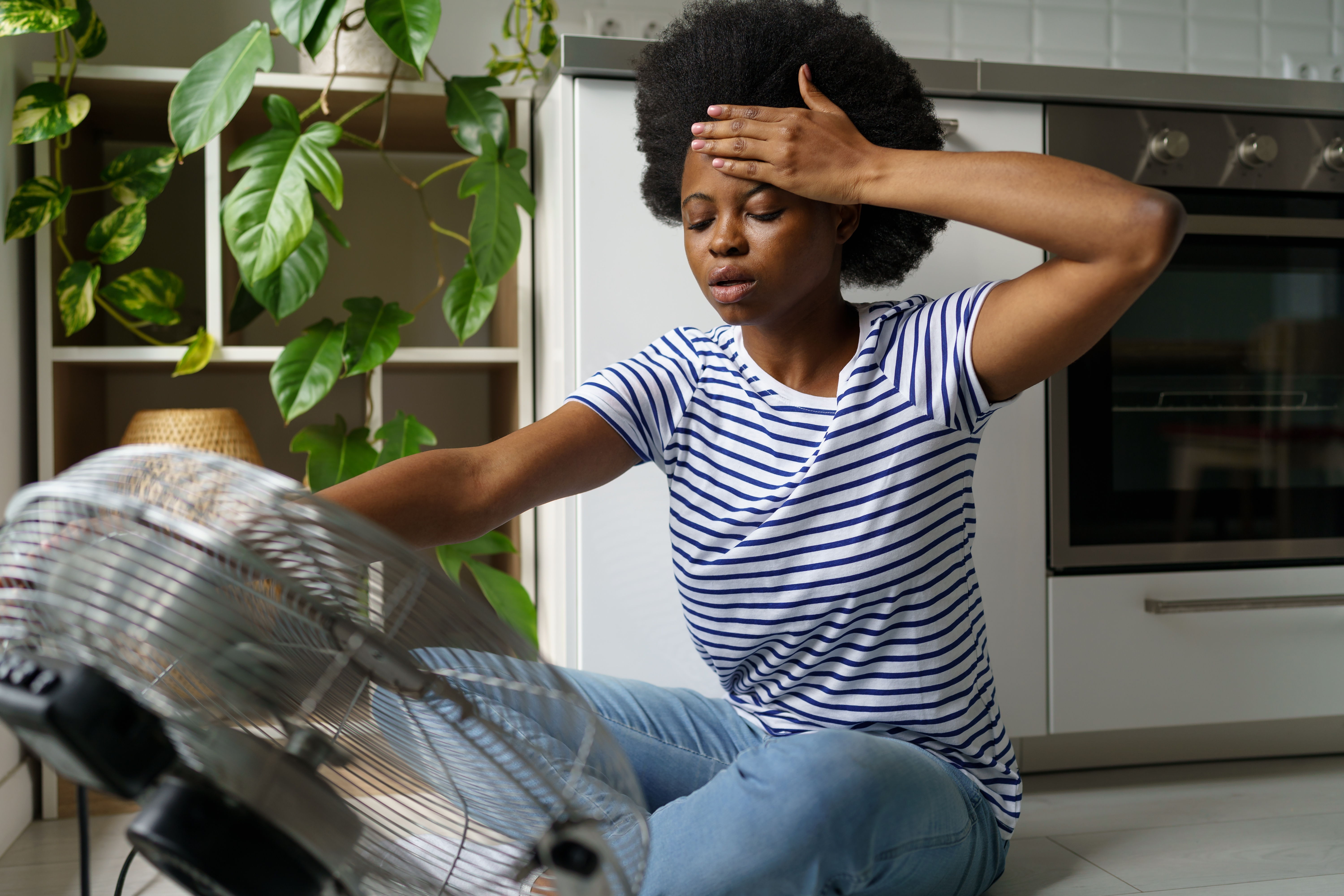 Person sitting near a fan, looking hot and distressed in a kitchen.