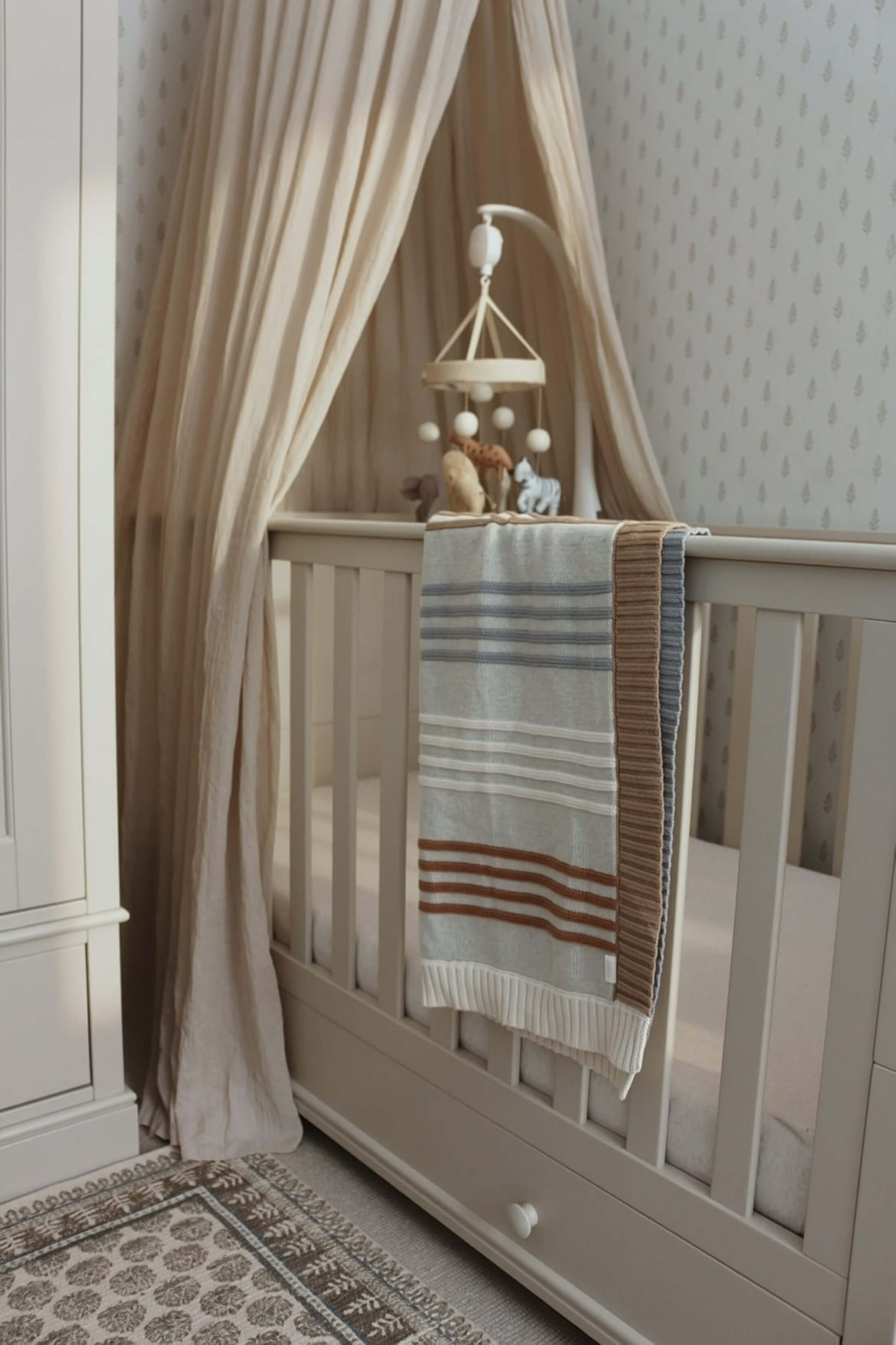A cozy nursery with a crib, blanket, and mobile.