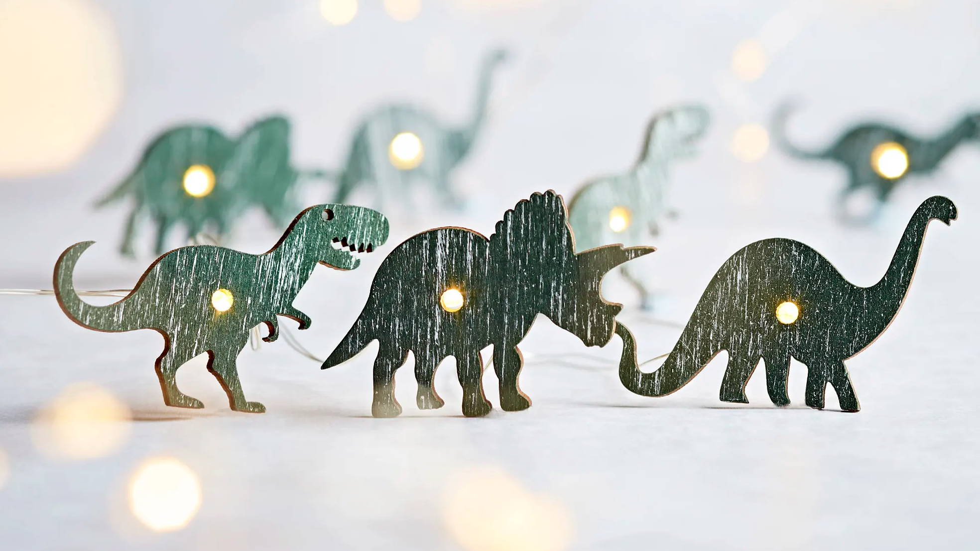 Close up of green dinosaurs fairy lights on a white surface.