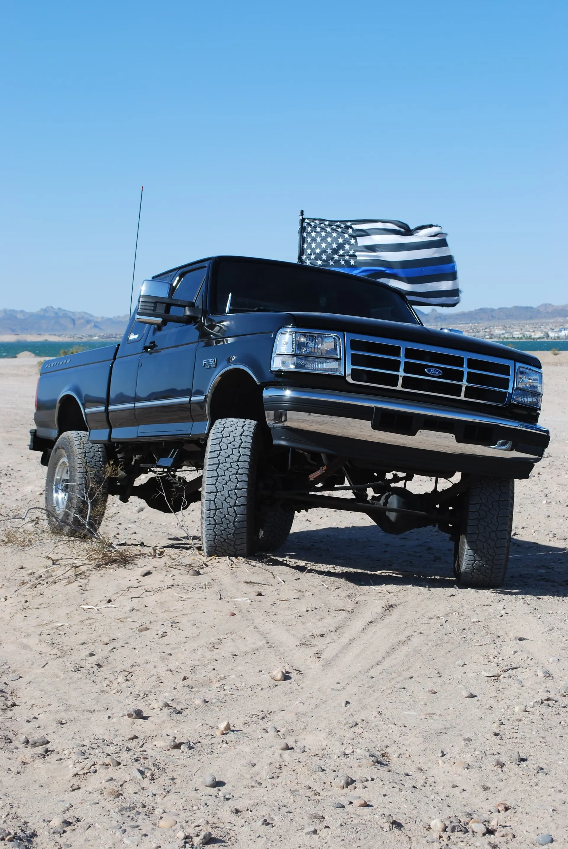 Noah's lifted black 1997 Ford F250 with Thin Blue Line flag parked in a desert landscape